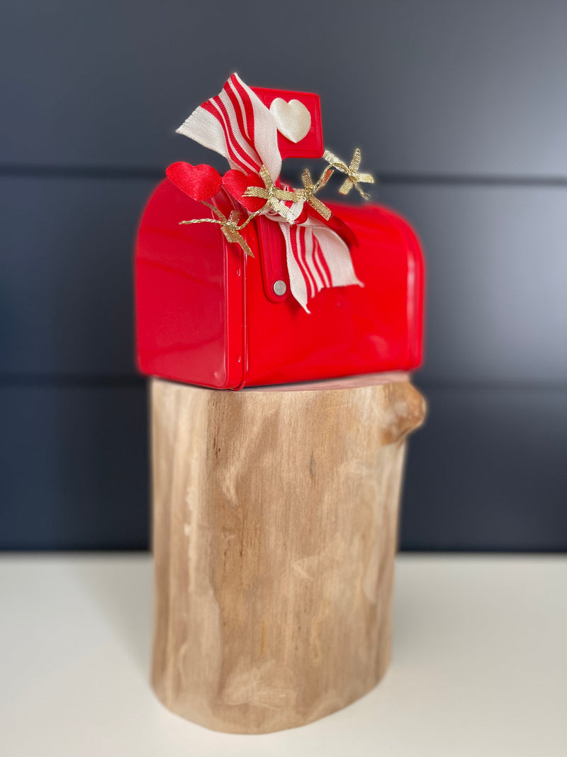 Three-quarter view of red Cupid’s mailbox with fabric hearts, red-and-white ribbon and gold star accents on a wood pedestal