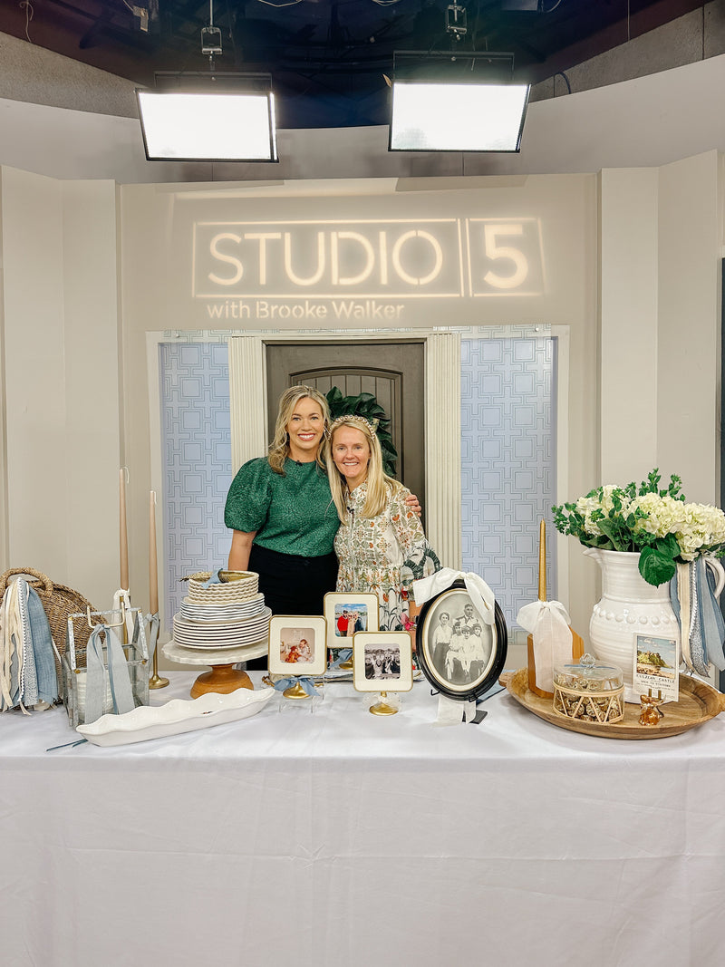Two women pose beside a ribbon display table beneath the Studio 5 with Brooke Walker sign