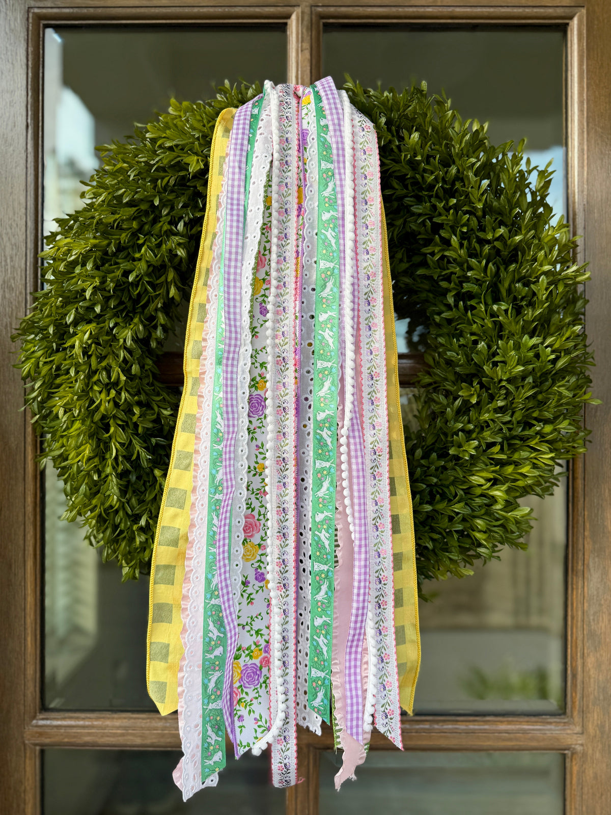 Front view of 27-inch wired spring ribbons draped over a boxwood wreath on a wood door, pastel floral, gingham and lace