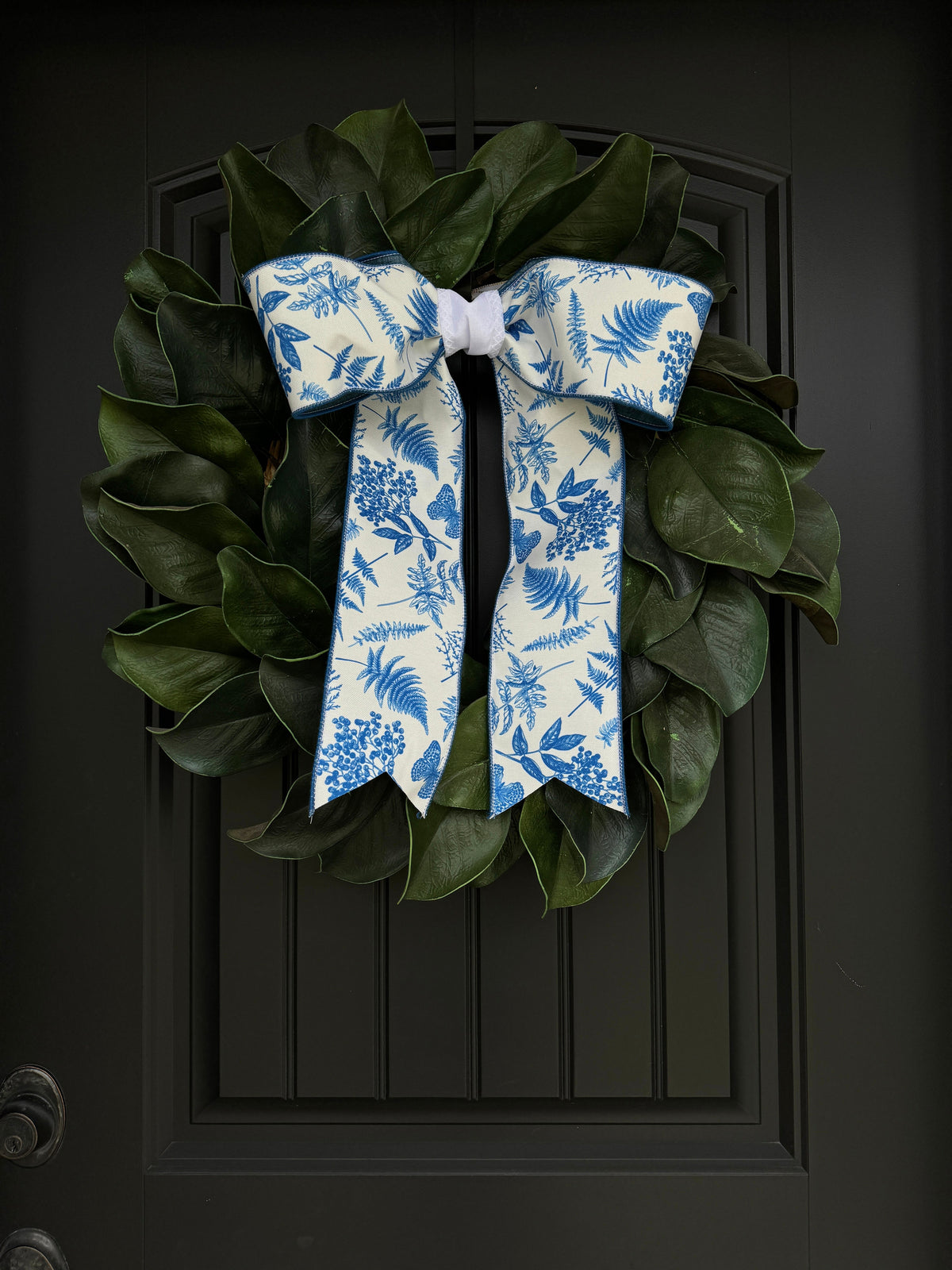 Blue botanical bow decorates a leafy wreath on a black front door for a summer entrance
