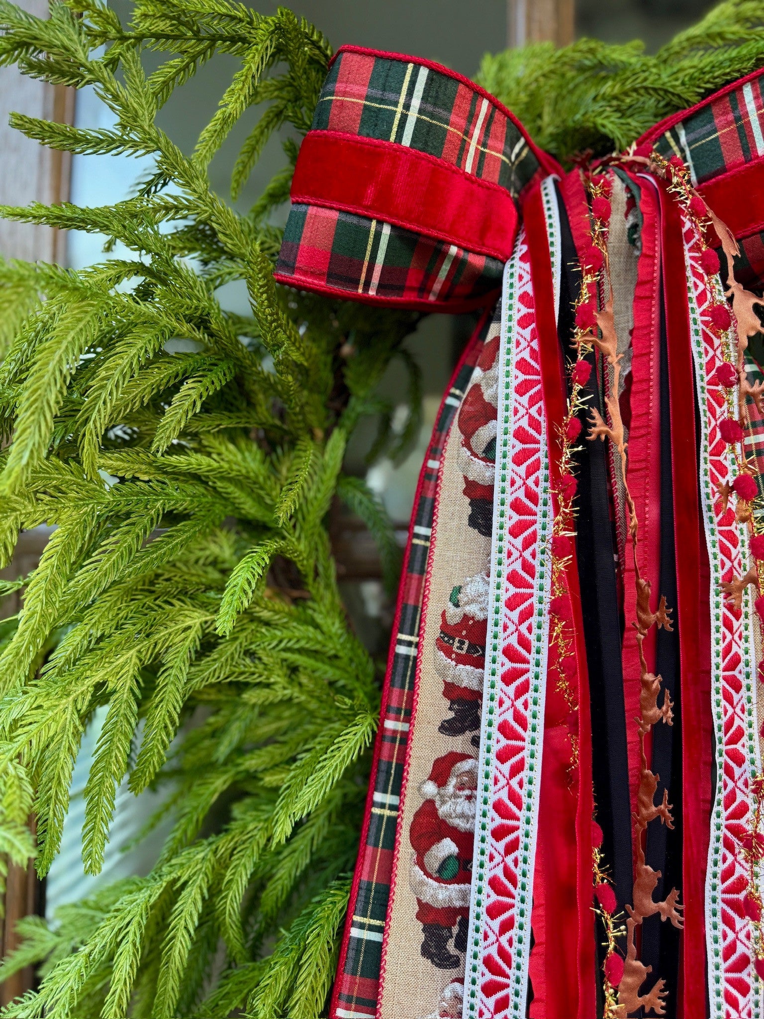 Red and green tartan bow with red velvet and Santa and reindeer ribbons on an evergreen wreath