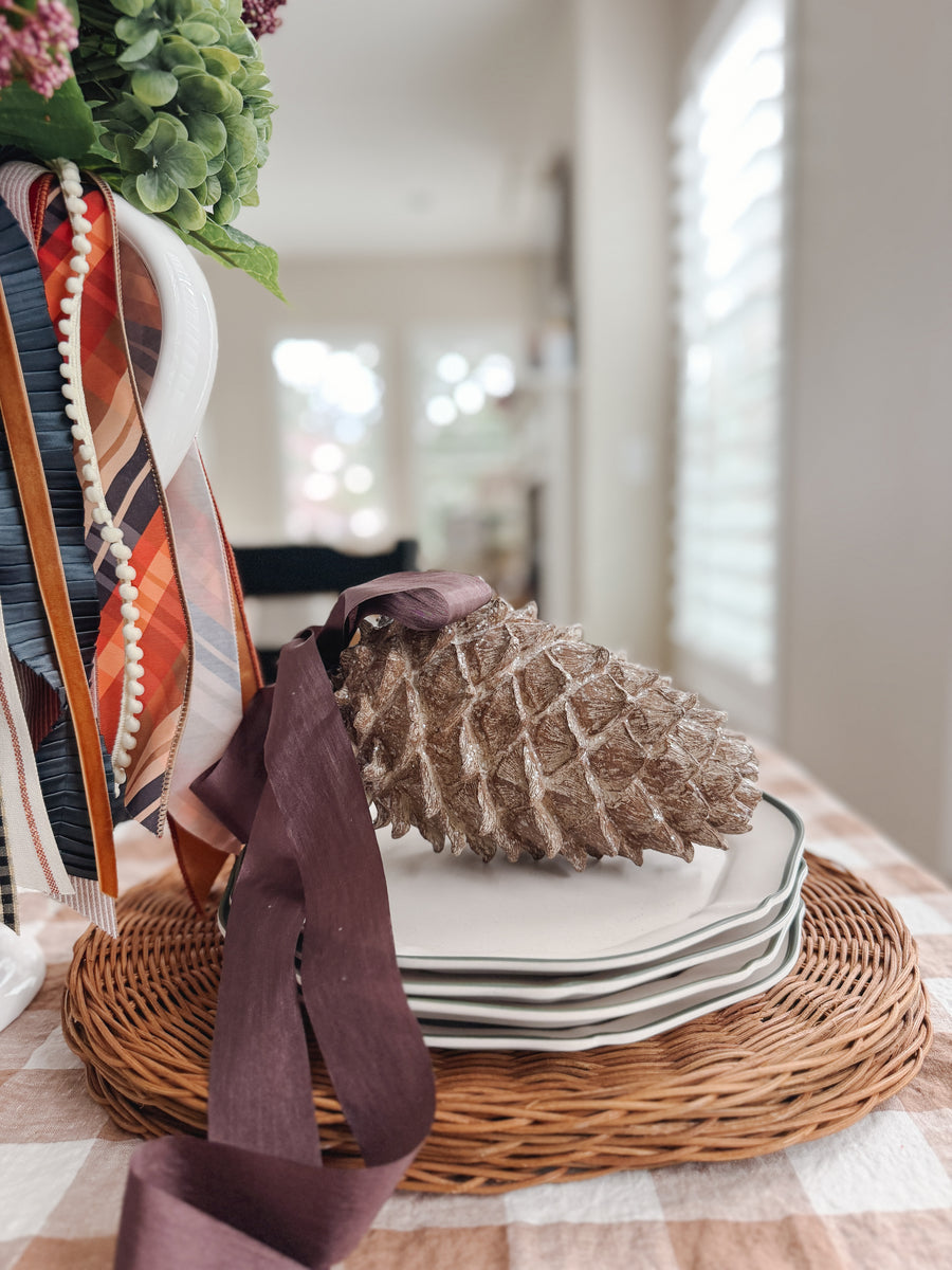 Side view of Woodland Pinecone showcasing glittered brown scales and a burgundy ribbon on stacked plates